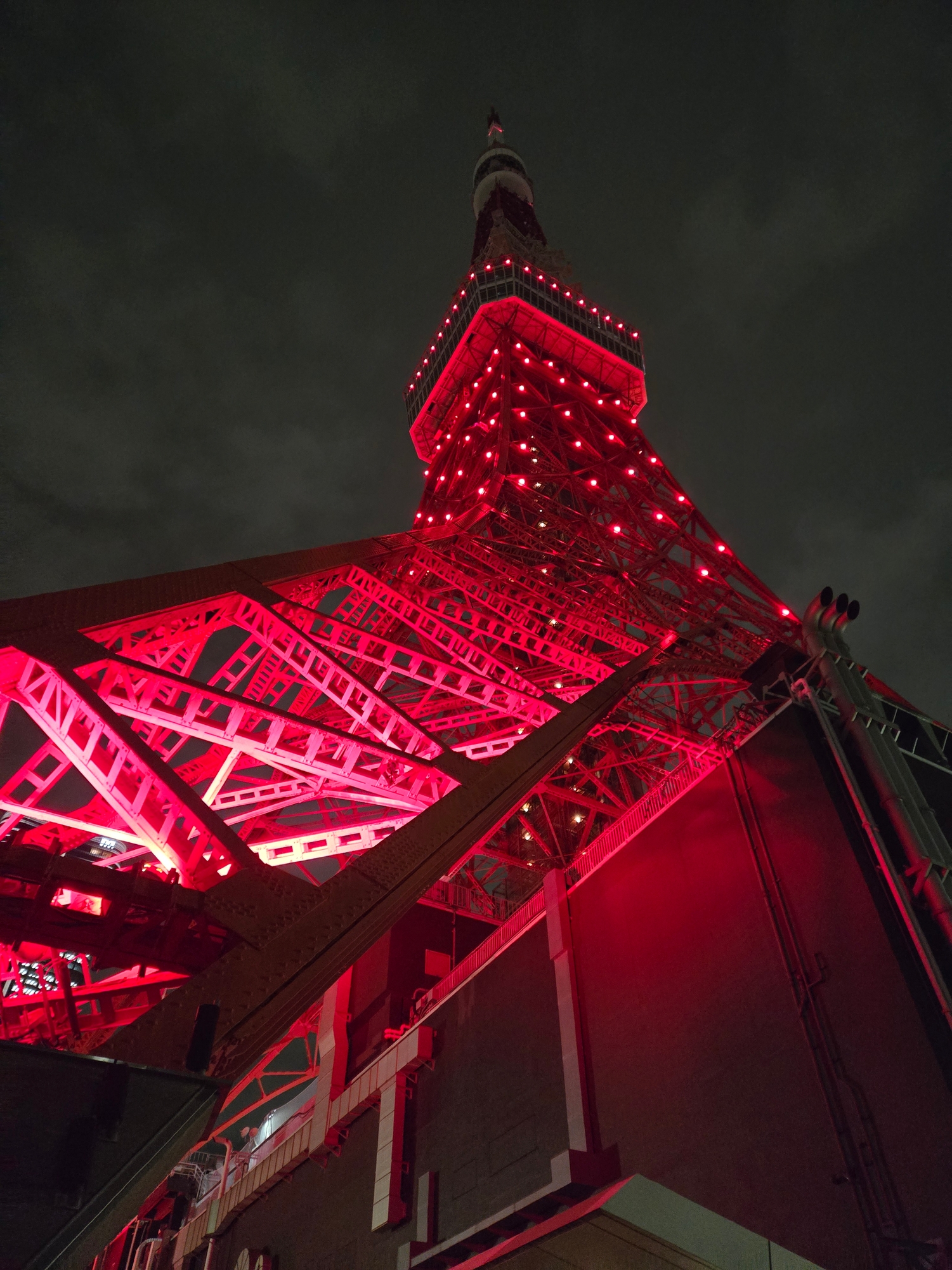 A photo of Tokyo Tower seen from street level, lit up with an ominous red colour, at night.