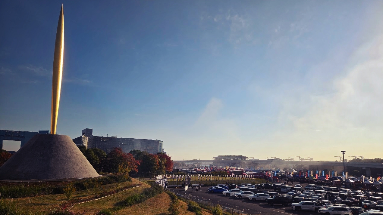 A photo of a gold spike on a pedestal overlooking a large carpark.