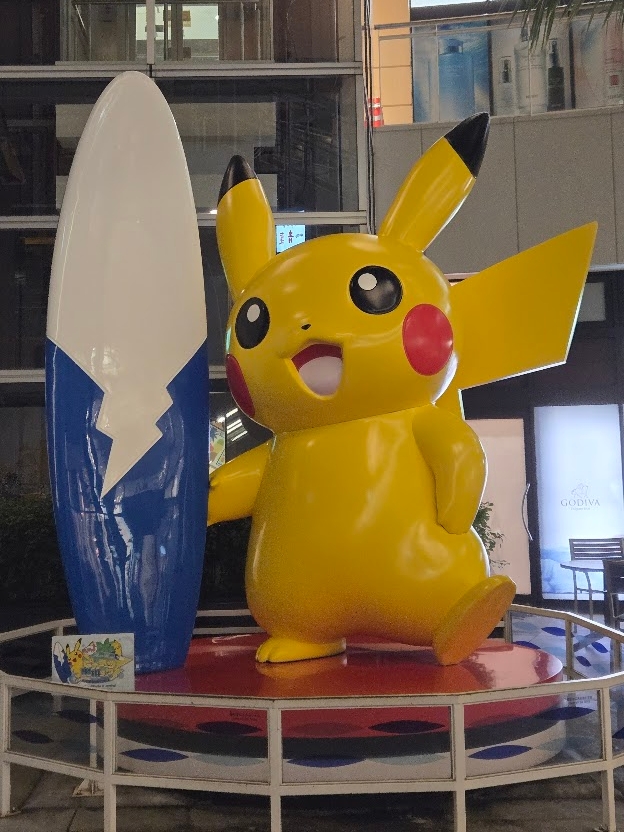 A photo of the Tokyo Bay Pokemon statue, feating a Pikachu standing next to and holding a surfboard.